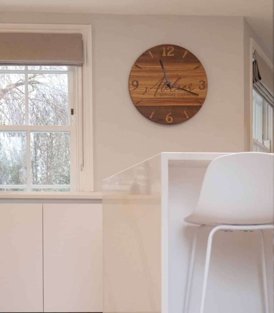 freshly painted kitchen in white, with brown wall clock and a table and stool featuring.