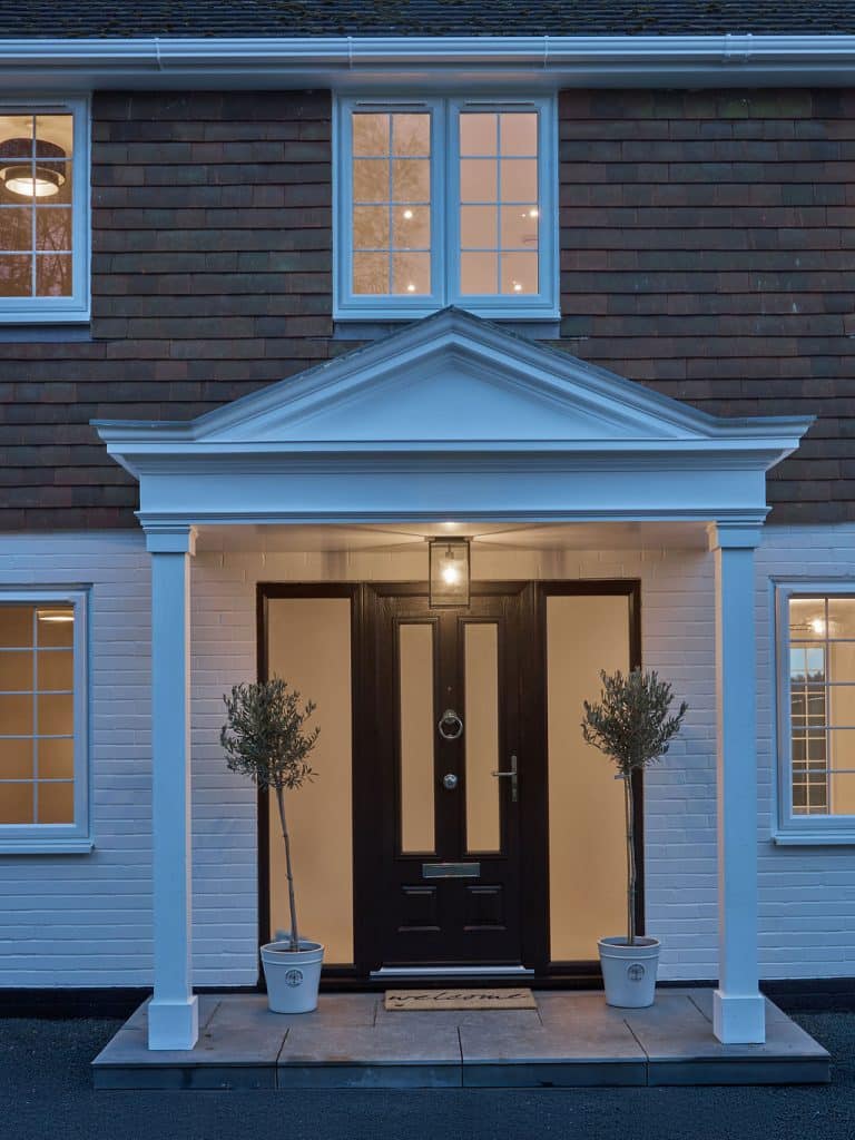 Front porch with outdoor light on in evening setting with two olive trees besides black front door
