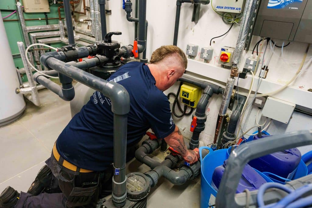 maintenance facilities manager wearing blue presence and co top perfoming plumbing check